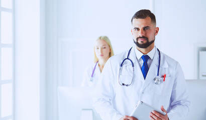 Obraz premium Confident smiling doctor posing and looking at camera with arms crossed, medical staff working on the background