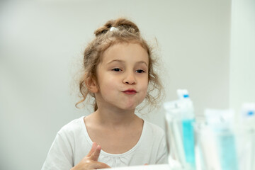 A little cute girl washes her face and looks at the mirror in the bathroom.