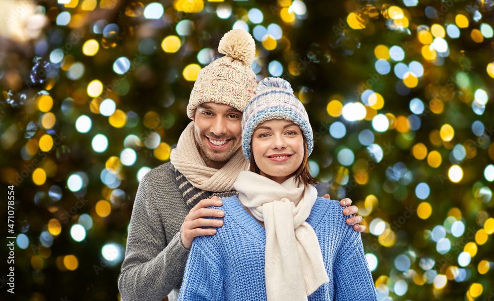 Poster people and winter holidays concept - happy couple in knitted hats and scarves over christmas lights background