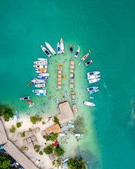 birds eye view of island with docked boats and massive party on the beach - obrazy, fototapety, plakaty