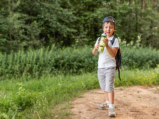 Thirsty boy holds in hands reusable green bottle with pure water. Summer outdoor recreation....