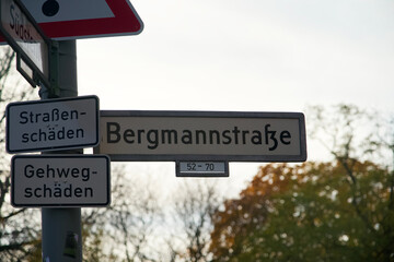 German Street Sign of Bergmannstrasse with additional Signs saying Roadway Damage and Sidewalk Damage