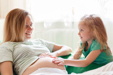 Happy daughter gently touches hug mom's pregnant belly. Portrait of daughter kid child and smiling pregnant mother. A parent's tenderness and love in family