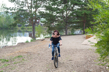 Naklejka premium Happy smiling brunette rides a bike in city park by the river.