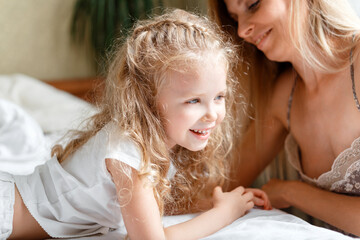 Portrait of daughter and mother spend morning together at home. Beautiful child girl Caucasian kid with mom in bed. Loving caring mom makes child wake up