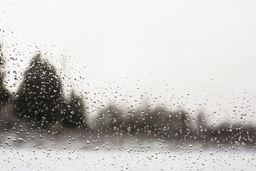 View through glass with water drops - blurred background with trees - depressive view from the windows at bad weather, winter