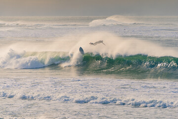 A airborne surfer diving through the spray of a large crashing wave