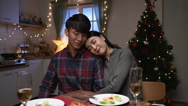 Beautiful passionate couple having romantic dinner at home celebrating christmas at night. young woman and husband hugging together by dining table with delicious xmas meal