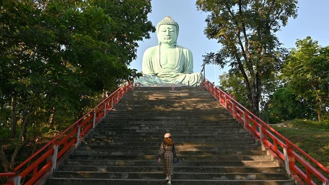Asian tourist woman walking on the stairs to see beautiful Big Buddha statue in traditional Japanese style located in Wat Phra That Doi Phra Chan temple in Lampang province, Thailand.