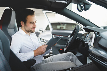 Successful caucasian young businessman in formal clothes checking reading information options on clipboard about new car, buying expensive automobile at auto dealer store