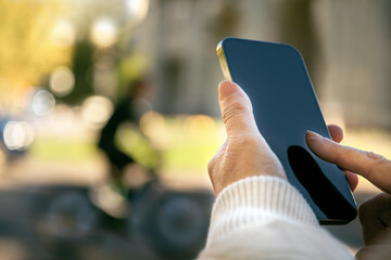 Woman's hand holding a mobile and making a message in the street