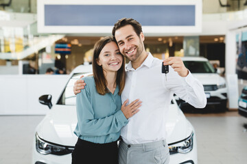 Happy young family holding car keys after buying new automobile at dealer shop store. Heterosexual...