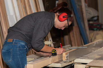 Young woman carpenter taking measurement of a wooden plank