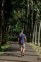 Fototapeta na wymiar Boy walking through tropical garden full of palm trees - back view