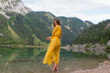 Young beautiful girl in a light yellow dress by the lake in the mountains