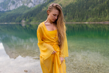 Young beautiful girl in a light yellow dress by the lake in the mountains