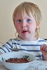 Little boy is having breakfast with chocolate balls with milk