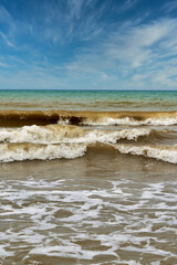 Large waves with foam on the sea coast against the background of the sky