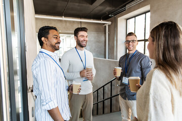 business, people and corporate concept - happy smiling colleagues with name tags drinking takeaway coffee at office