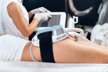 Woman lying receiving epilation laser treatment and anticellulite massage on buttock on the spa...