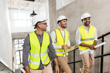 architecture, construction business and people concept - male architects in helmets with blueprints and clipboard walking upstairs at office