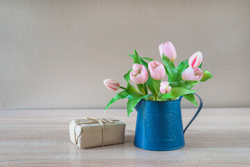 Holiday concept. Bouquet of pink tulips in blue vase and handmade gift box on wooden background