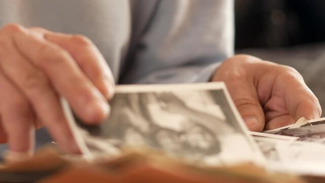 Close-up of an elderly man sifting through old black-white photos, memories of youth. Old photo in the hands of an elderly man recalling his youth. Selective focus, shallow depth of field
