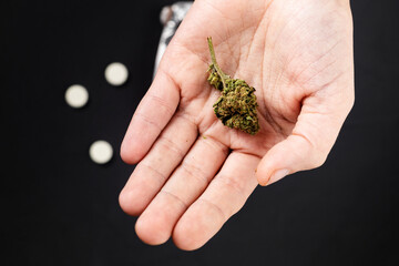 Marijuana bud on a female hand on the background of pills out of focus. Medical cannabis as an alternative to drugs concept.