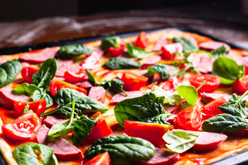 Pizza background. Cooking pizza with sausage, tomatoes, green leaves close-up.