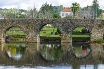 Fototapeta premium Beautiful park with river and stone bridge in the village of Serta - Portugal. Autumn folliage trees reflecting on the water. Roman ancient bridge over the river