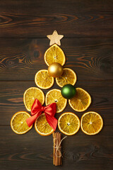 Christmas tree made of dry oranges and Christmas baubles on a dark brown wooden background. Creative festive concept.