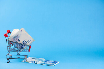 Israel money shekel banknotes in shopping cart on blue background. Exchange Rates and buy sell currency concept.