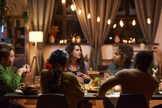 Group of friends talking to each other at dining table during a meeting at dinner party at home
