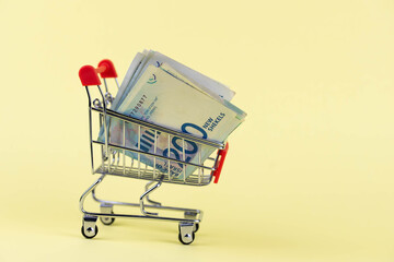 Israel money shekel banknotes in shopping cart on yellow background. Exchange Rates and buy sell...