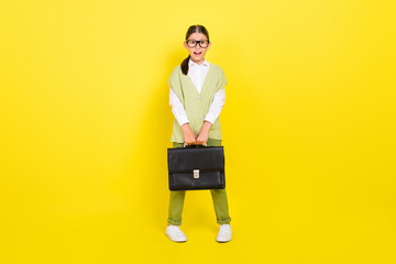 Full length body size view of attractive amazed cheerful girl holding briefcase isolated over bright yellow color background - obrazy, fototapety, plakaty