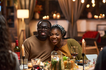 Portrait of happy African couple smiling at camera while sitting at dining table in the room
