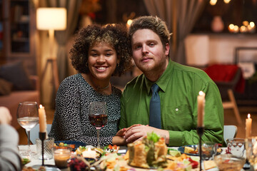 Portrait of multiethnic young couple smiling at camera while having a romantic dinner at the table