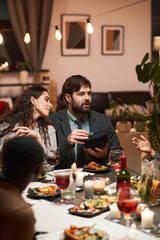 Young people sitting at festive dining table and talking, they having dinner in the living room
