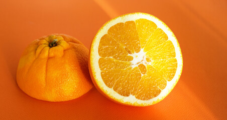 Ripe juicy orange cut into halves and sun glare on an orange background. Close-up. Selective focus. Copy space for text