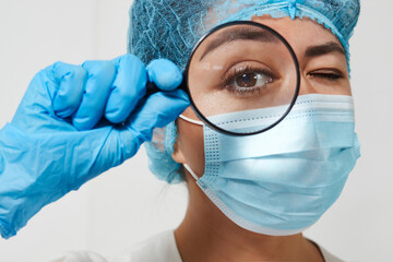 Young woman doctor with medical face mask and magnifier