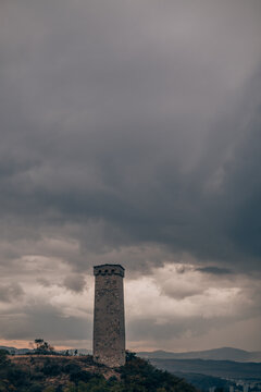 Large ancient stone tower stands on a hill in the forest. Mountain view with tragic sky. Old architecture, historical heritage, medieval tower