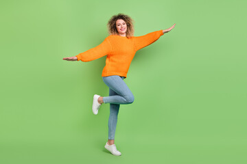 Fototapeta na wymiar Full size photo of cool blond wavy hairdo lady fly wear orange pullover jeans sneakers isolated on green color background