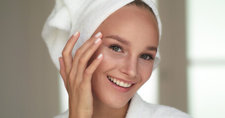 Close up of Smiling Beautiful Young Woman Touching her Soft Fresh Face Skin after Applying Cream or Skincare Treatment Procedure.