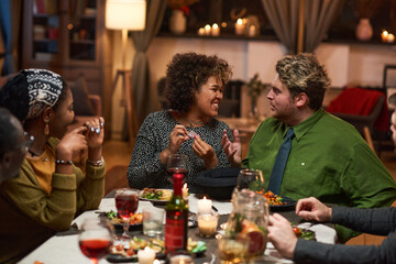 Group of friends having fun while sitting at dining table during dinner party