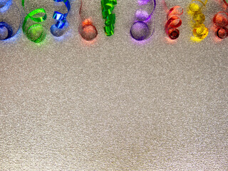 Closeup festive curly garlands as upper border on shiny shimmering silver sequined background.Colorful metal ribbons.Christmas,New Year,birthday foil serpentine decoration.Horizontal banner,copy space