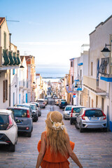 Blonde girl walking in an Italian village under the sun. Sant'antioco, Sardinia, Italy. - 471101767