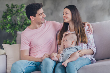 Fototapeta premium Portrait of attractive careful cheerful full family cuddling baby sitting on divan hugging resting free time at home indoors