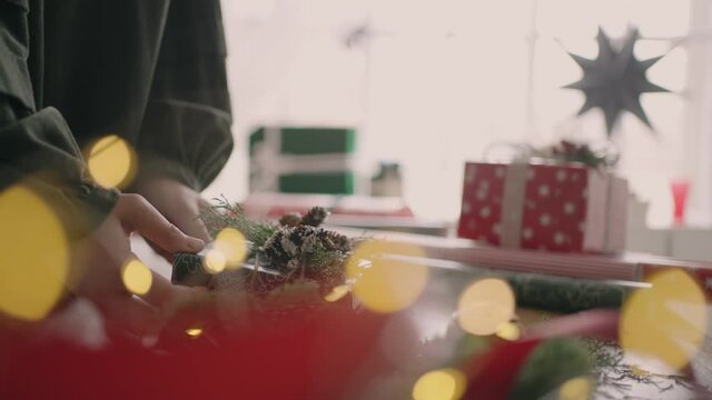 Crop hands decorating wrapped box with string. Female packing cardboard gift box on wooden table with various decorative items prepared for Christmas celebration. Detail female hands tying rope