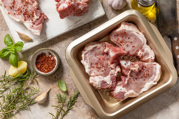 Fresh raw pork loin on the bone with spices and marinade on a stone tabletop, preparation for baking or barbecue. Top view flat lay background.