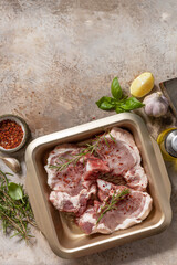 Fresh raw pork loin on the bone with spices and marinade on a stone tabletop, preparation for baking or barbecue. Top view flat lay background. Copy space.